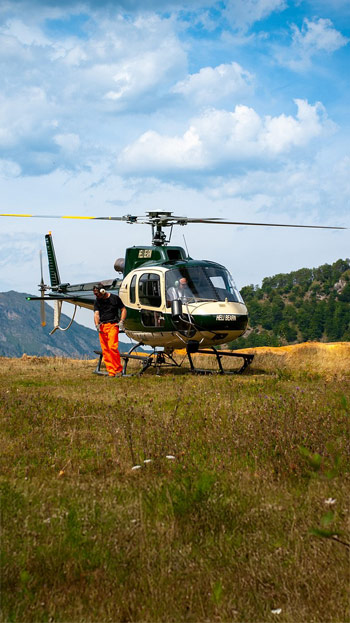 helicopter on grassy hill with man in orange pants standing in front